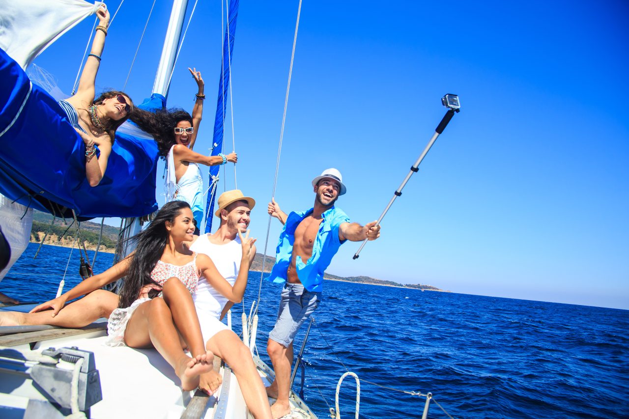 Group of cheerful friends having fun on a yacht, making selfie. All with casual clothes. Blue sea and sky on background.